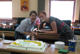 two students laugh with cake on their face. The cake reads, "Welcome to OCES at W&M"