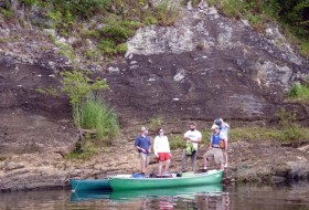On the outcrop, the field crew poses with part of the flotilla at the James River’s edge.