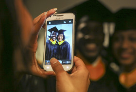 Picture of two students on a phone at Commencement in regalia