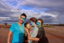 A family (3 girls, one boy) smiles and embraces with blue paint all over them