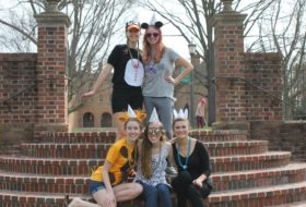 5 students wearing party hats pose on the steps in the sunken garden.