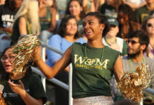 Female student with gold pompoms cheering at a Tribe football game