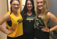 Three girls smiling in the hallway of their freshman dorm, decked out in William & Mary clothing and green and gold face paint.
