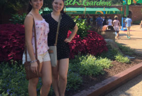 two girls pose in front of a bush with a cut-off view of the Busch Gardens sign in the backdrop