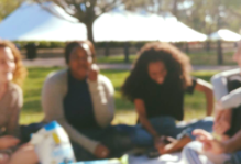 Four college seniors sit outside enjoying a picnic and time together.