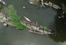 An outcrop of rock in the James River river with members of the team and their canoes in the water and standing on the outcrop