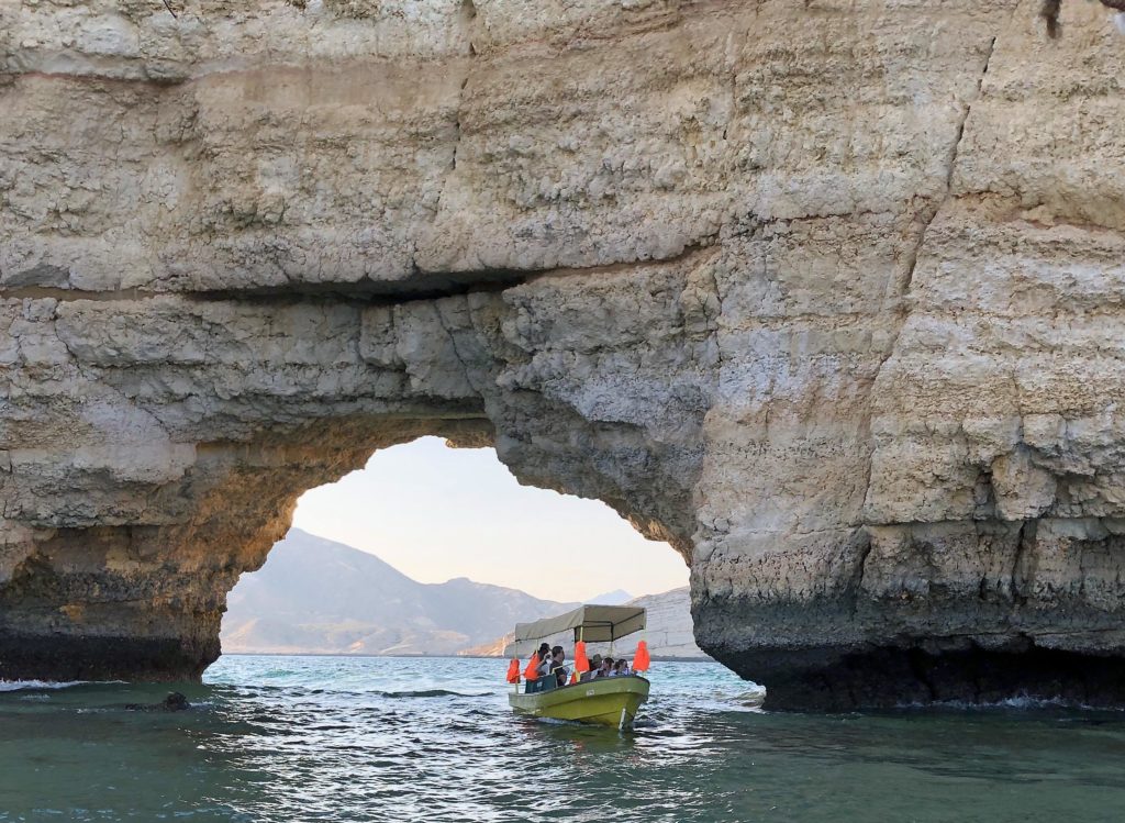 W&M students on a boat near Qantab, Oman going through an arched opening in the high rocks.