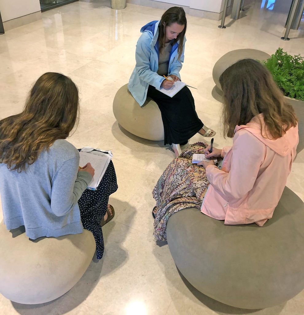 Students sitting on rounded stone shaped seats writing in notebooks.