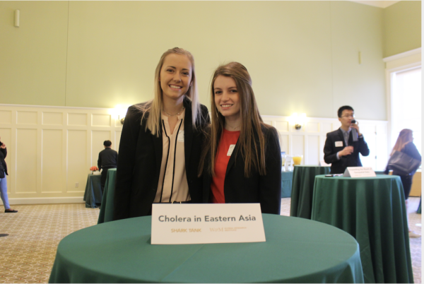 Two students standing at a cocktail table in Brinkley Commons with a placard that reads Cholera in Eastern Asia.