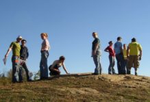 W&M students at Hidden Rock Park, standing atop an outcrop with blue sky behind them.