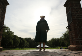 A silhouette of a graduate in commencement robes and mortar board standing at the top of the steps to the Sunken Garden
