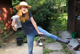 Margaret wearing black spotted rain boots and a straw hat posing in her yard.