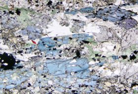 A blueschist thin section showing angular fractured shapes in green, blue, purple, white and gray.