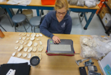 Mary Lawrence Young working on their computer at a large work table with a collection of shells next to them.