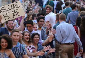 Crowd of cheering current students with hand drawn signs of welcome and outreached hands to give high fives to a procession of new students in the Wren Courtyard at Opening Convocation