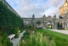 The quad at St Andrews in Scotland: lush green grass and bushes, with paths leading to grey stone arched walls