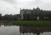 St Andrews Quad in Scotland. A stone building and its reflection on the wet ground, with a cloudy sky above.