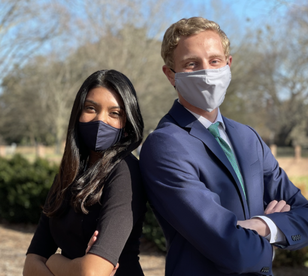 Two masked people, posed back to back with their arms crossed, in professional attire.