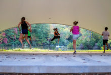 Several students in the air mid-jump during an outdoor BodyCombat FitWell Class at the Martha Wren Briggs Amphitheatre at Lake Matoaka