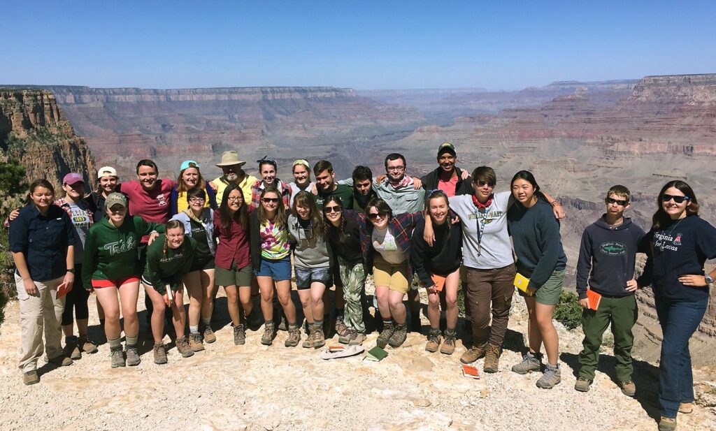 Twenty five students in outdoor gear posed with the Grand Canyon and blue skies behind them.