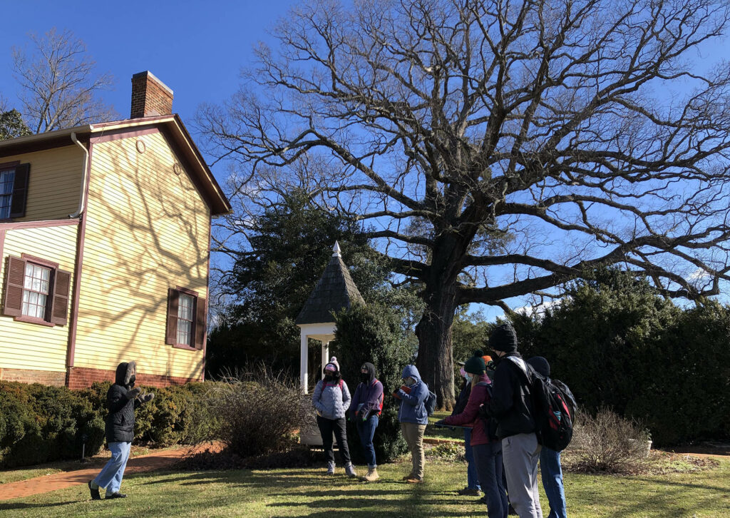 Six students at the historic Highland estate bundled up from the cold weather and grouped next to a large, two story house.