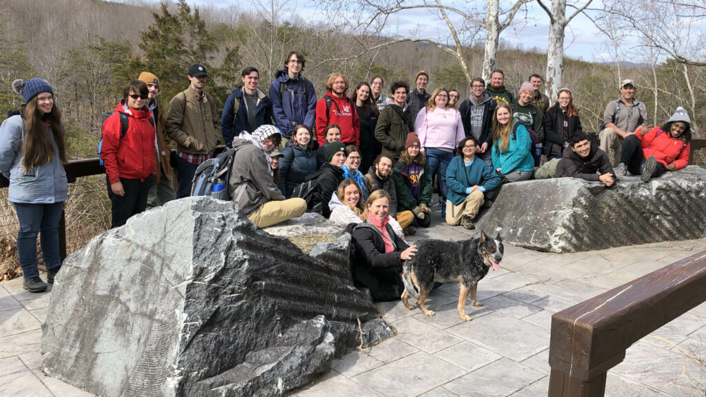 About 3 dozen smiling participants and one dog standing and sitting around quarried rocks