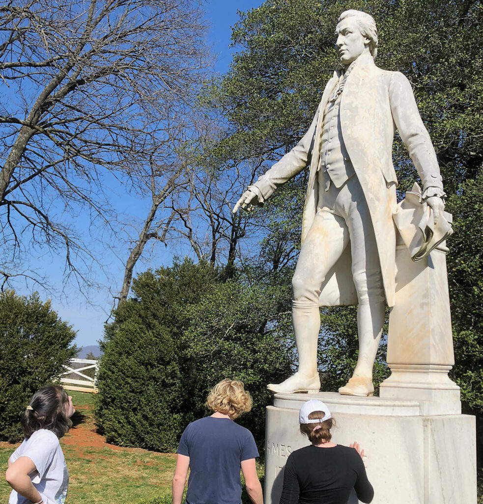Marble statue of James Monroe with W&M students examine the rock texture.