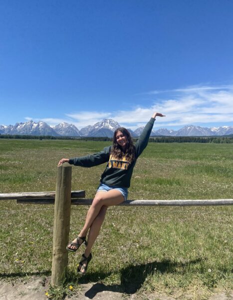 Person sitting on a fence rail with snow-capped mountains in the background