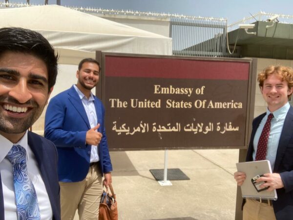 Three smiling people posed with an Embassy of The United States of America sign in English and Arabic