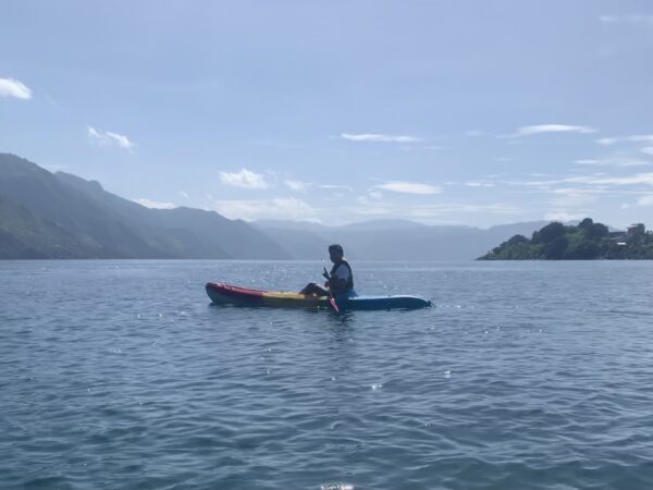 A person in a kayak in the foreground of an expansive lake view with mountains in the distance