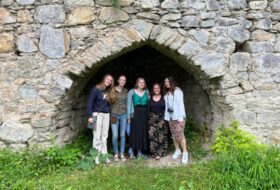 Five smiling people posed together under the arched opening of a large niched in a rock wall