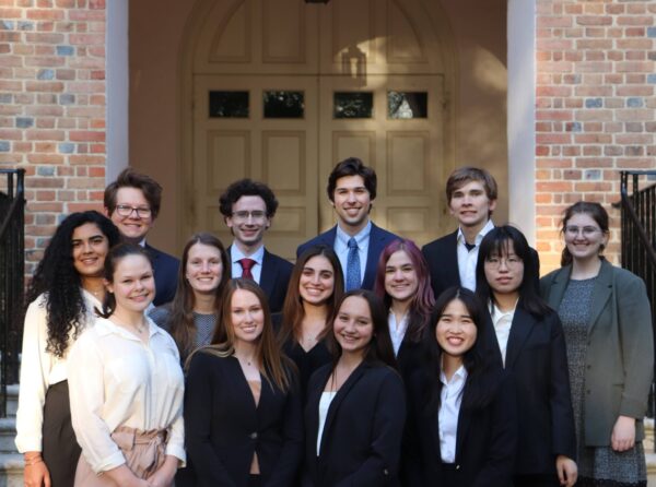 Fourteen smiling students posed in professional attire on the steps of the Wren Building