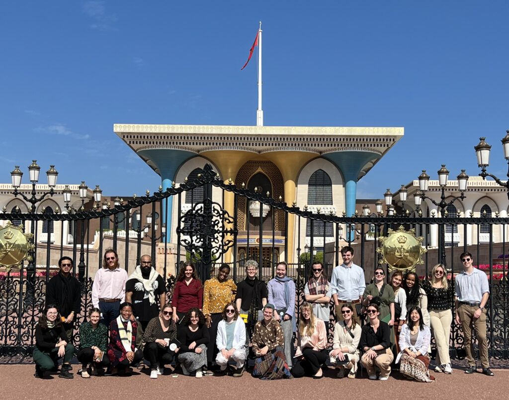 A group of two dozen people posed in front of a black fence with a palace in the background
