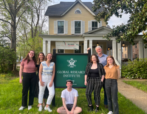 Six students pose with Mike Tierney by the Global Research Institute sign. On the house in the background hangs a sign that reads: Big ideas live here.