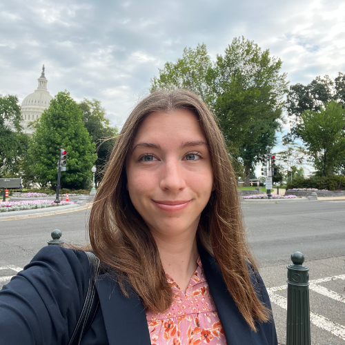 Selfie on a street corner with trees, garden beds and the U.S. Capitol building in the distant background